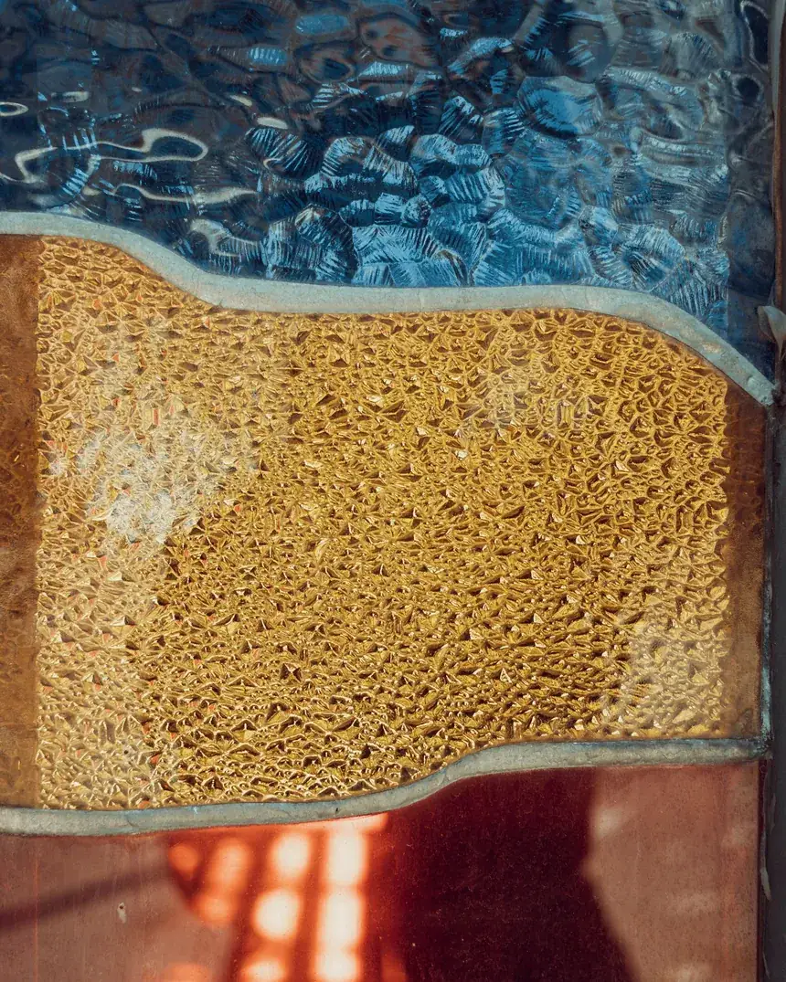 Detalle de una superficie de vidrio fundido con capas de color cálido y azul y textura irregular